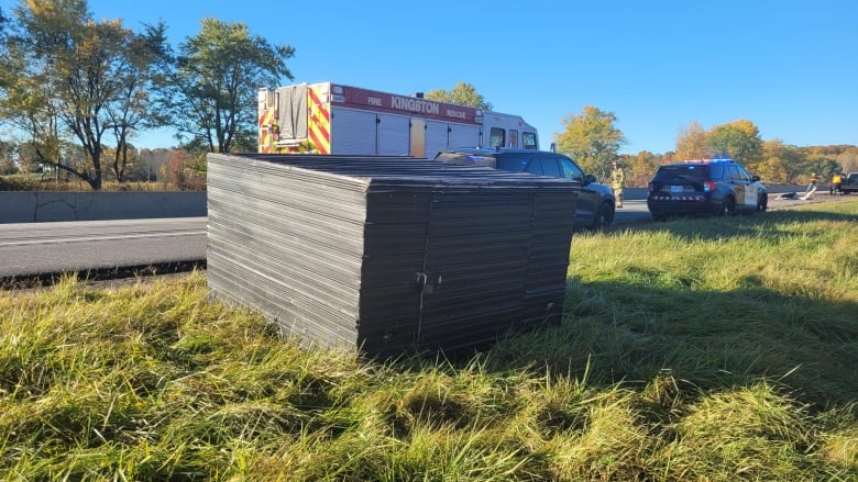 Homemade trailer sitting in the grass on the side of the highway. Two police cars and a fire truck sit behind it.