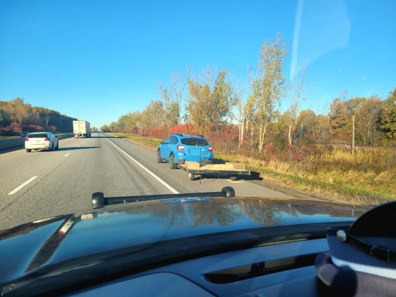 Blue Subaru with an empty trailer bed behind it. Photo taken from a police cruiser.