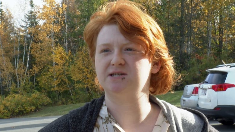 A young man with red hair, talking in a parking lot with trees in the background.