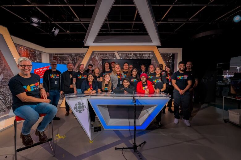 a group of people pose for a photo in front of a tv studio desk