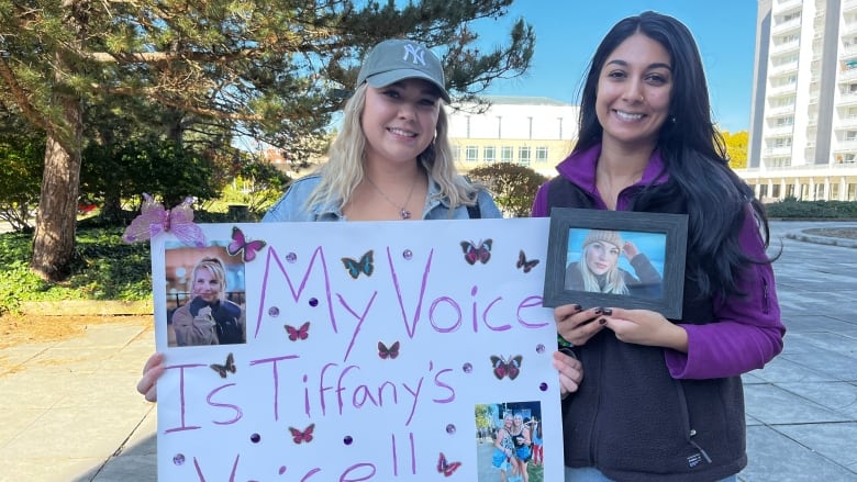 Two woman smile at the camera. One holds a poster that says 