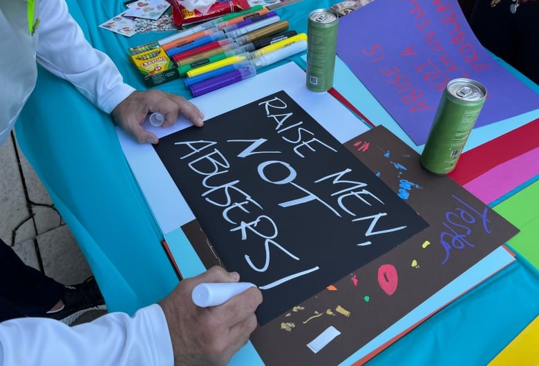 A close-up shot of hands writing on a poster. The poster says 