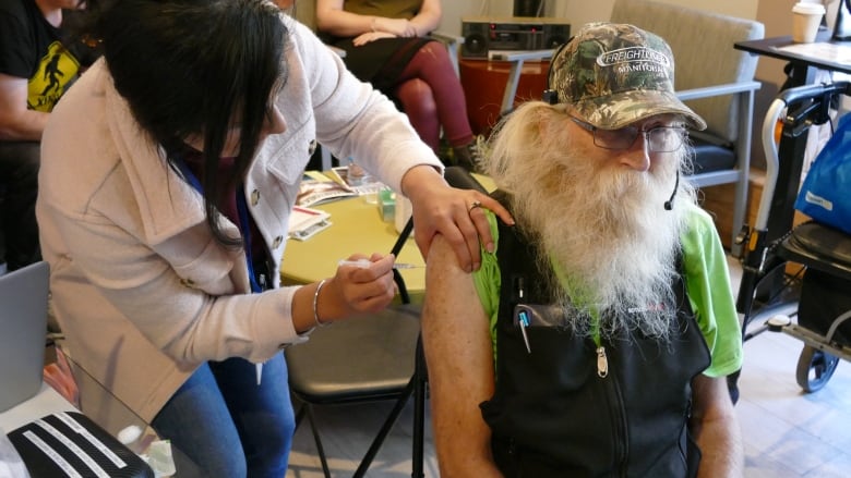 A doctor gives a shot to a man seated in a chair. 