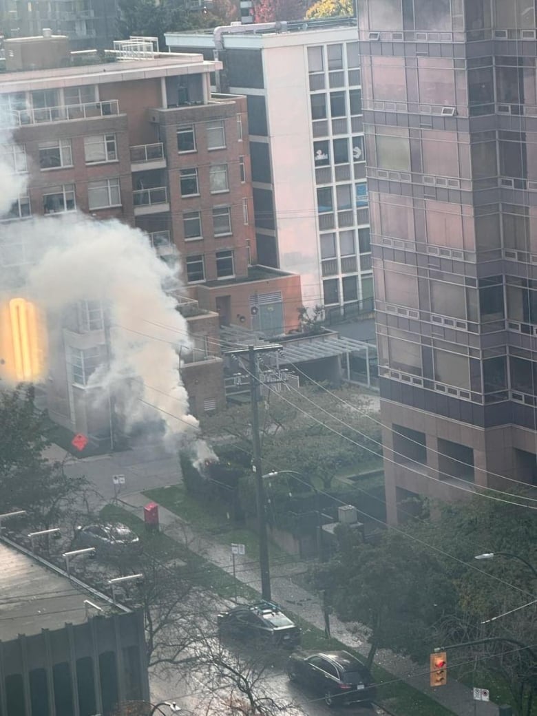 Smoke emanates from shrubbery beneath an apartment building.