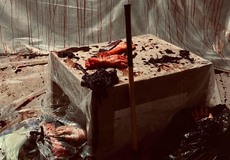 Fake severed human hands with bloody axe on a chopping block, bloody curtain in background. 