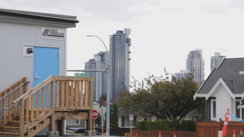 A closeup of a portable classroom with a blue door and several highrises clustered in the background.