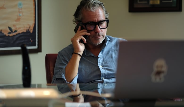 A man sits at a desk talking on his cellphone.