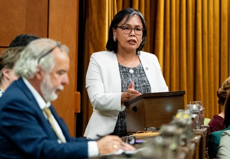 An Indigenous woman speaks in the House of Commons as others look on.