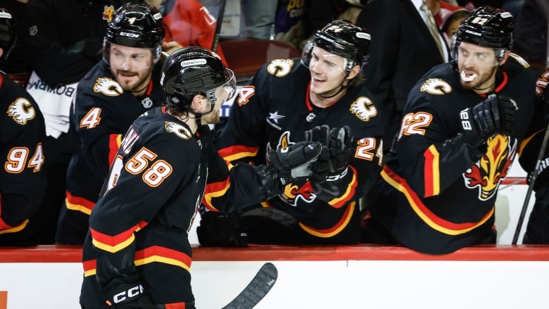 a hockey player in red and black and yellow skates past his teammates on the bench as they celebrate 