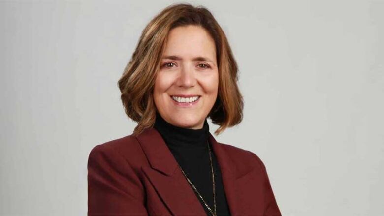 A smiling woman with brown hair, wearing a black turtleneck and burgundy blazer.