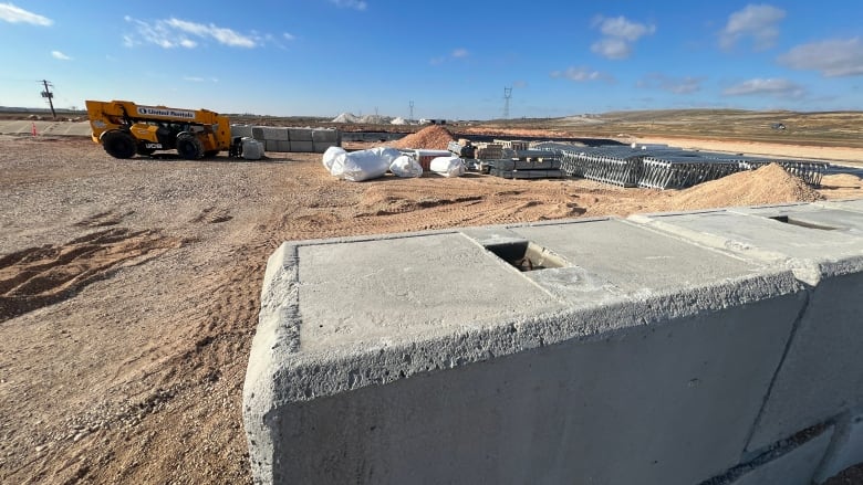 Concrete slabs and other building materials on a dirt surface with heavy equipment in the background. 