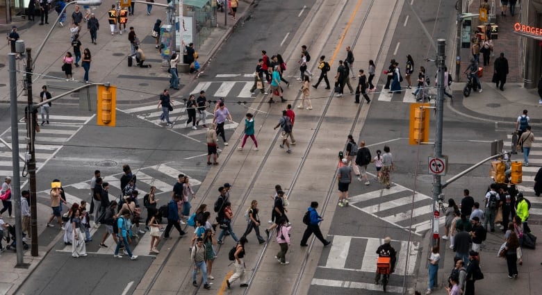 An aerial shot shows many people crossing the street at an X crossing in Toronto. 