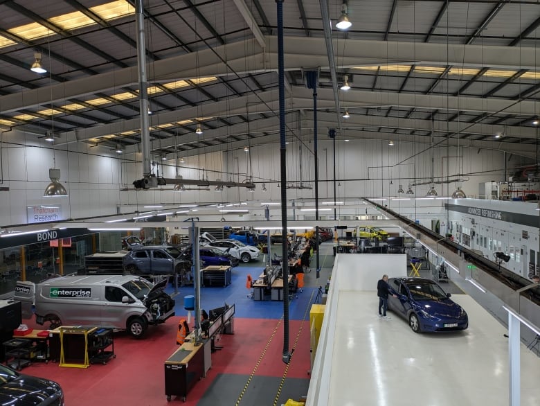 A high shot inside a warehouse-like building with cars and equipment scattered about.