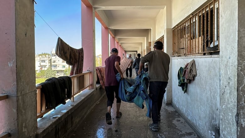 Two people carry a dead body wrapped in a blue blanket.