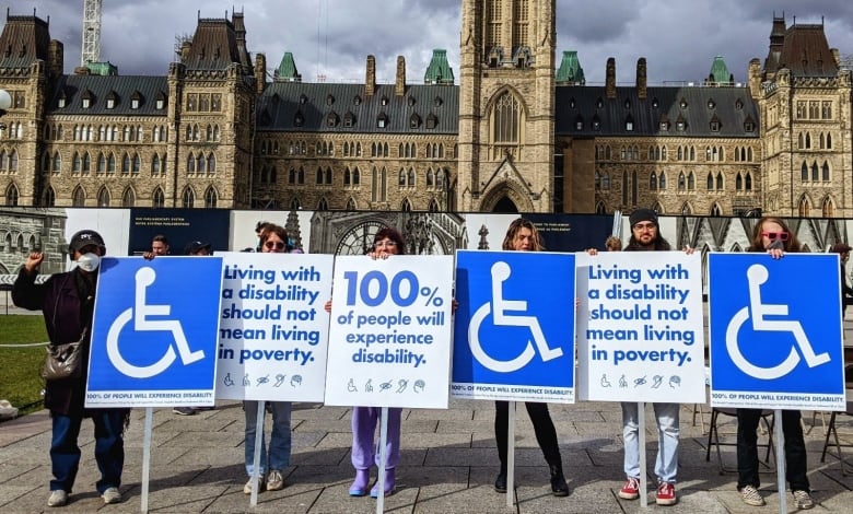 Six people holding various signs, standing on Parliament Hill.