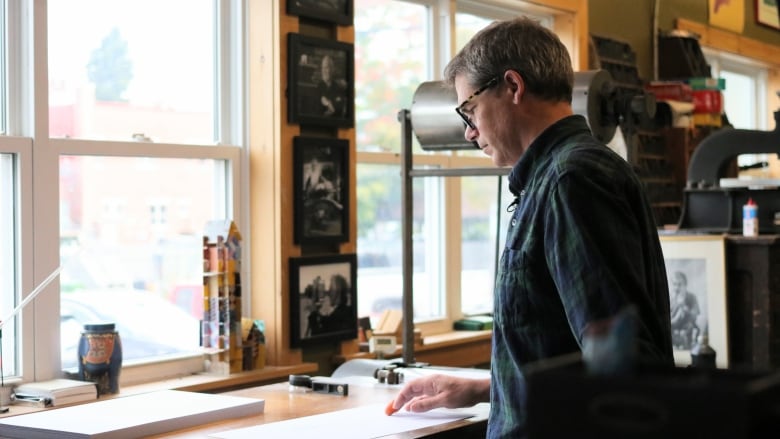 A person handles paper on a flat surface before feeding it into a printing machine. Windows are in front of the person.