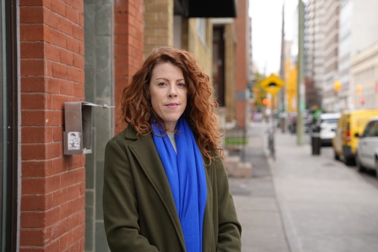 A woman with red hair standing against a brick wall outside.