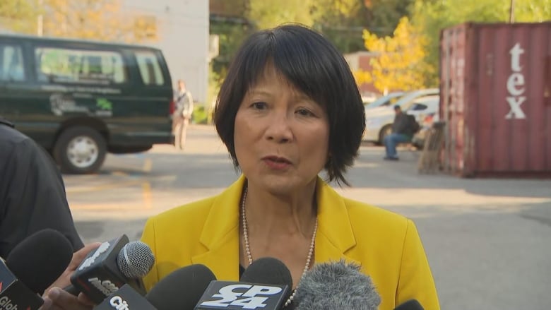  Toronto mayor Olivia Chow standing outside surrounded by microphones are reporters asked her questions 