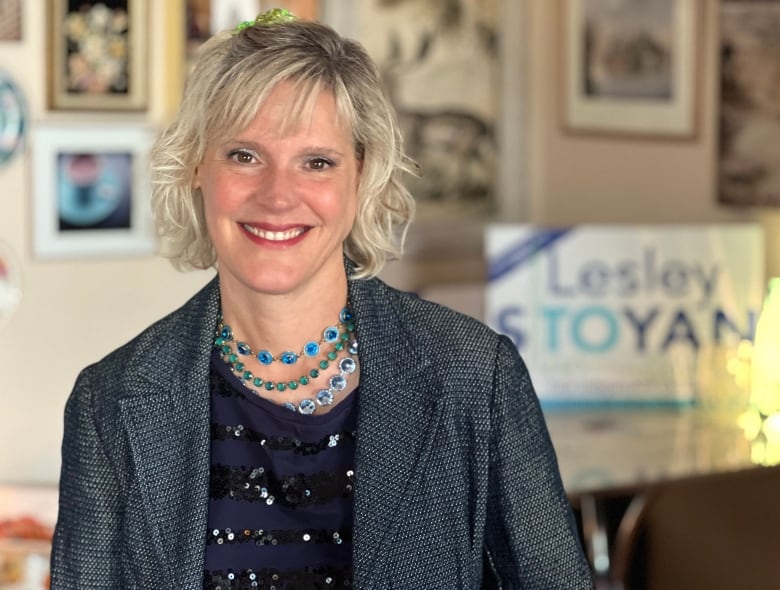 Woman in a dark suit coat sits in from of a campaign sign.