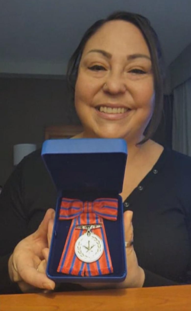 A silver-coloured medal with a blue and red ribbon tied in a bow sits in an ornamental box similar to a jewelry box.