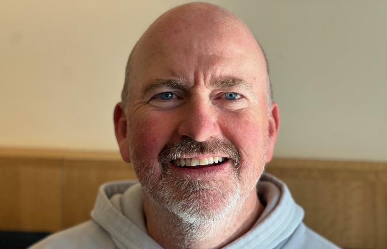 A bald man, with a grey goatee and wearing a grey hoodie, smiles.