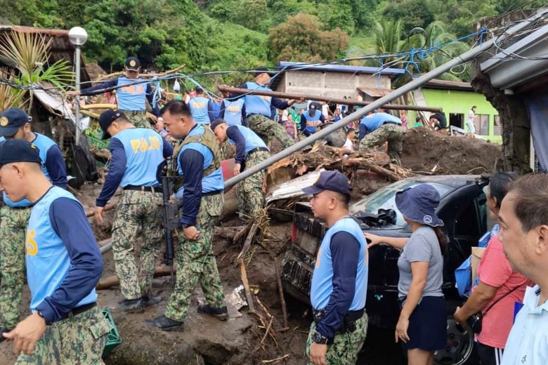 Several men wearing blue vests and camouflage pants walk in a muddy area that appears to be rural.