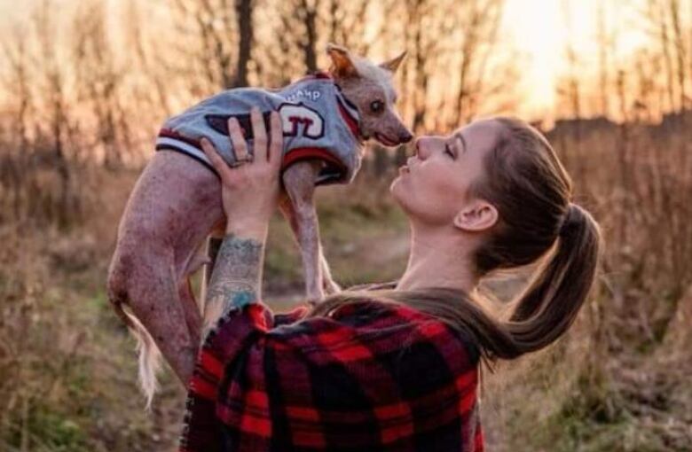 A woman holds up a dog to her face in a field. 