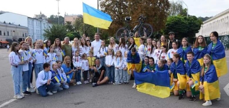 A group of people holding Ukrainian flags stand together. One holds a bicycle in the air above his head. 