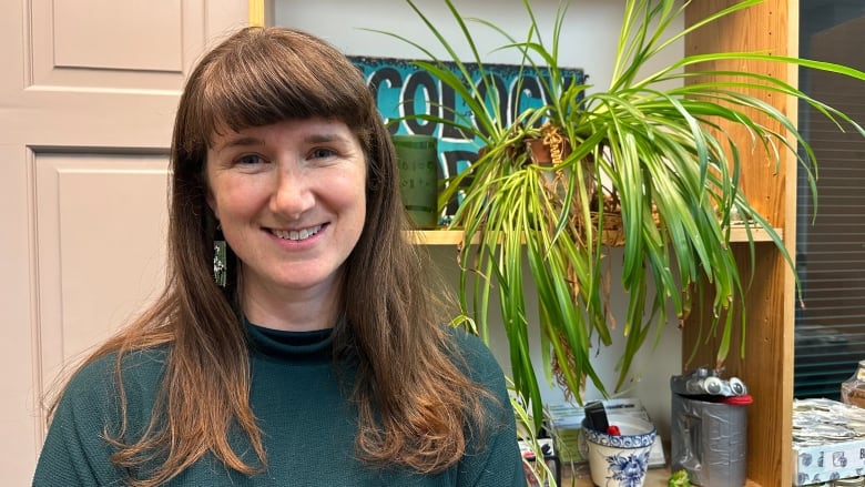 A woman in a green turtle neck next to a plant.