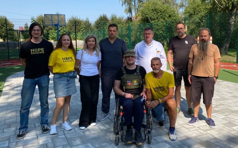 A group of people pose for a photo together in a courtyard. A man in front sits in a wheelchair. 