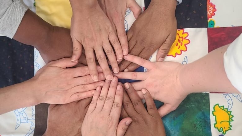 Hands join together above a colourful handmade quilt.