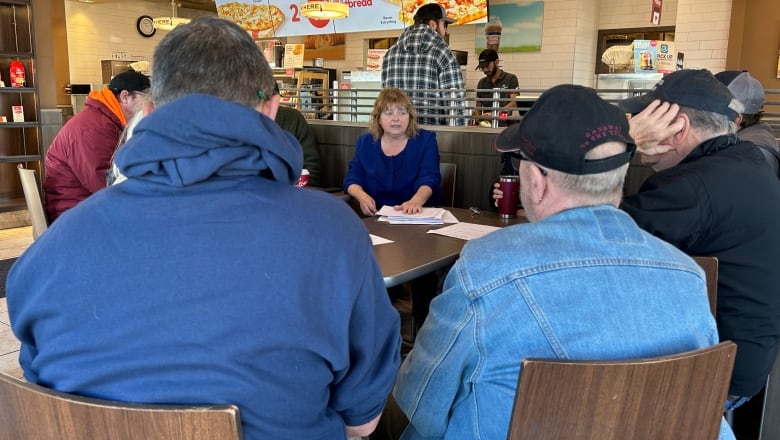 Roughly a dozen people sitting around a table at Tim Hortons