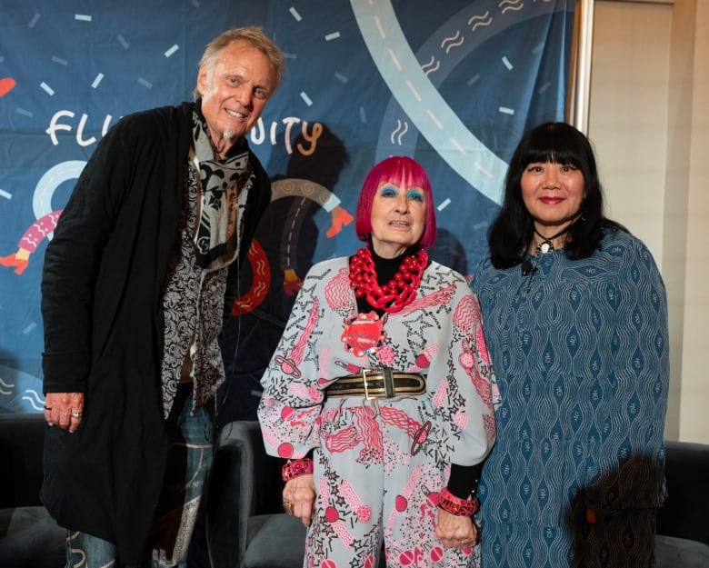 A man, a woman with pink hair and a woman with black hair pose for a photo.