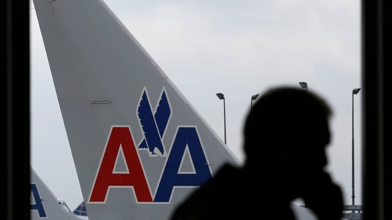 A man's silhouette is shown as he speaks on his cellphone at an airport, with a plane visible outside the window behind him.