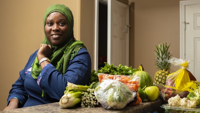 A woman sits by fresh fruit and vegetables.