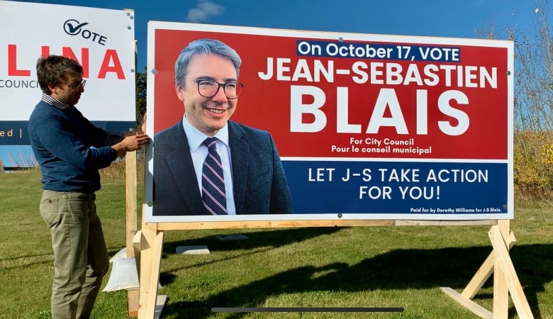 A man stands beside an election campaign sign.