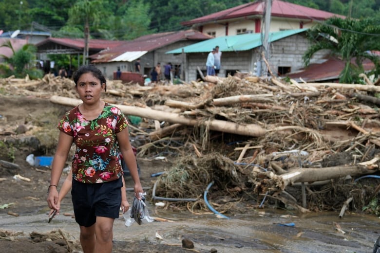 A person walks past toppled trees after a landslide. 