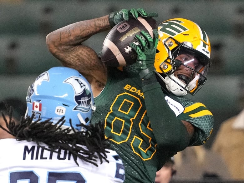 A football player in a green-and-yellow uniform catches a football, pinning the ball to their helmet.