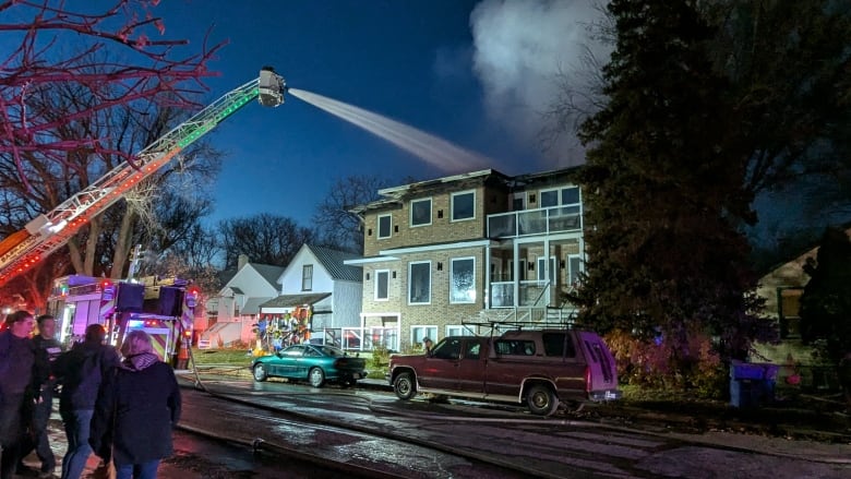 People looking across the street at a house being doused with water as smoke billows.