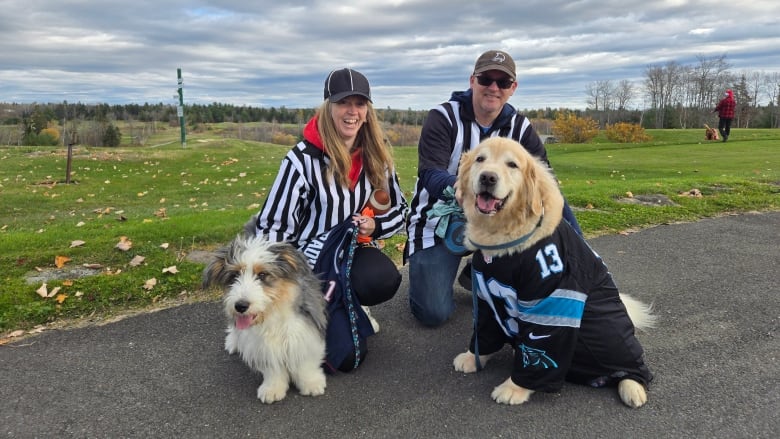 Two people smiling with their dogs, one wearing a jersey.