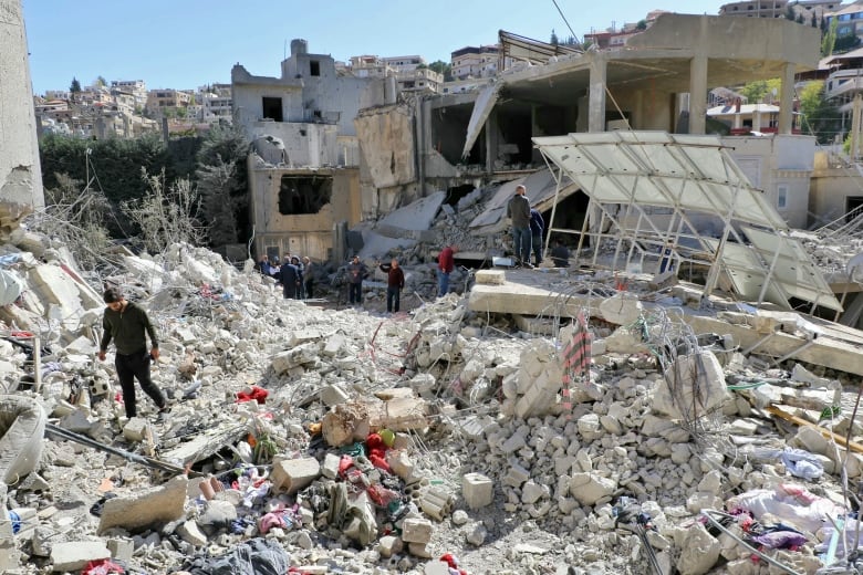 People inspect and navigate the rubble of a destroyed building.