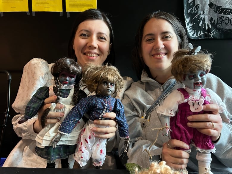 Two women with long dark hair holding up spooky looking dolls.