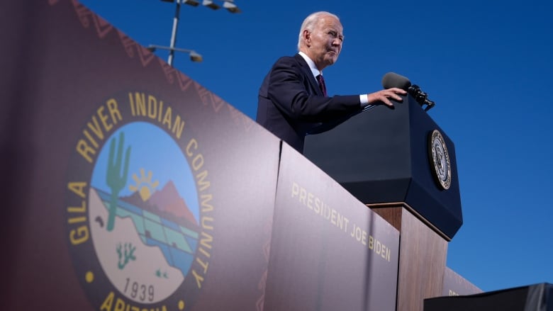 A man speaking in front of a podium on a stage with an emblem that reads: 'Gila River Indian Community  1939, Arizona.'