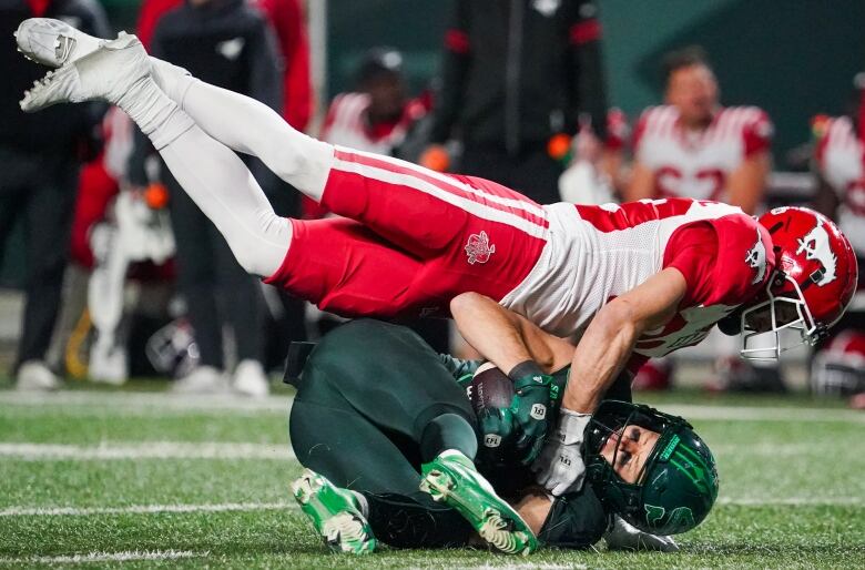 A football player lands on top of another player holding the ball on the ground.