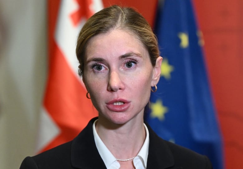 A person is pictured speaking while standing in front of flags.