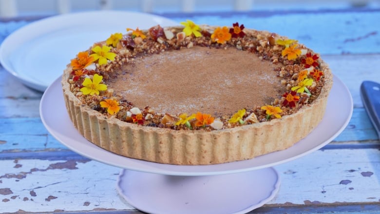 A tart dusted with cinnamon and rimmed with pieces of brittle and edible flowers.