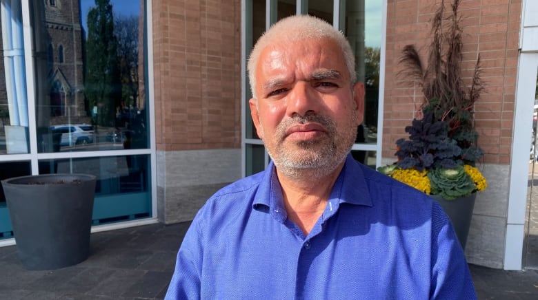 Close up photo of Azad Goyat wearing a blue shirt and standing in front of Brampton city hall. 