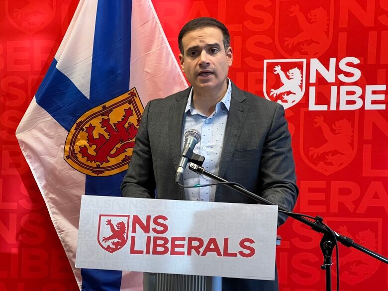 Man in suit stands at podium indoors.