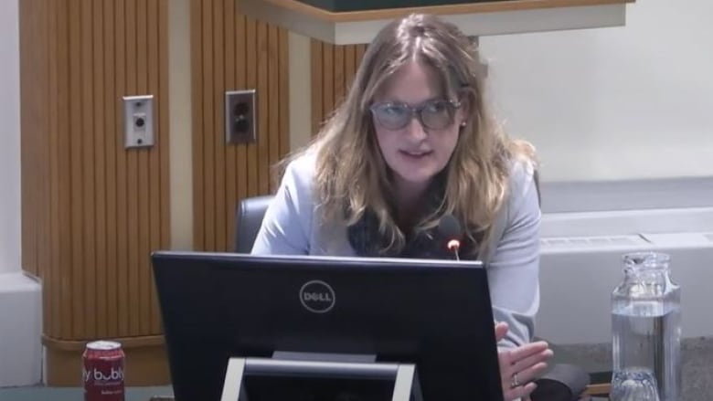 Woman speaking into microphone and sitting in front of computer screen in city council chambers