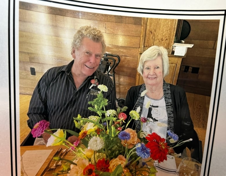 A photo of a woman and a man together, sitting at a table, with flowers in front of them.